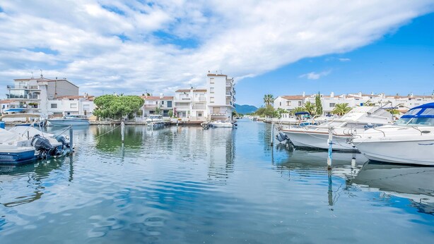 Un port de plaisance où sont amarrés des bateaux, entouré de bâtiments blancs aux toits recouverts de tuiles rouges, et un ciel dégagé.