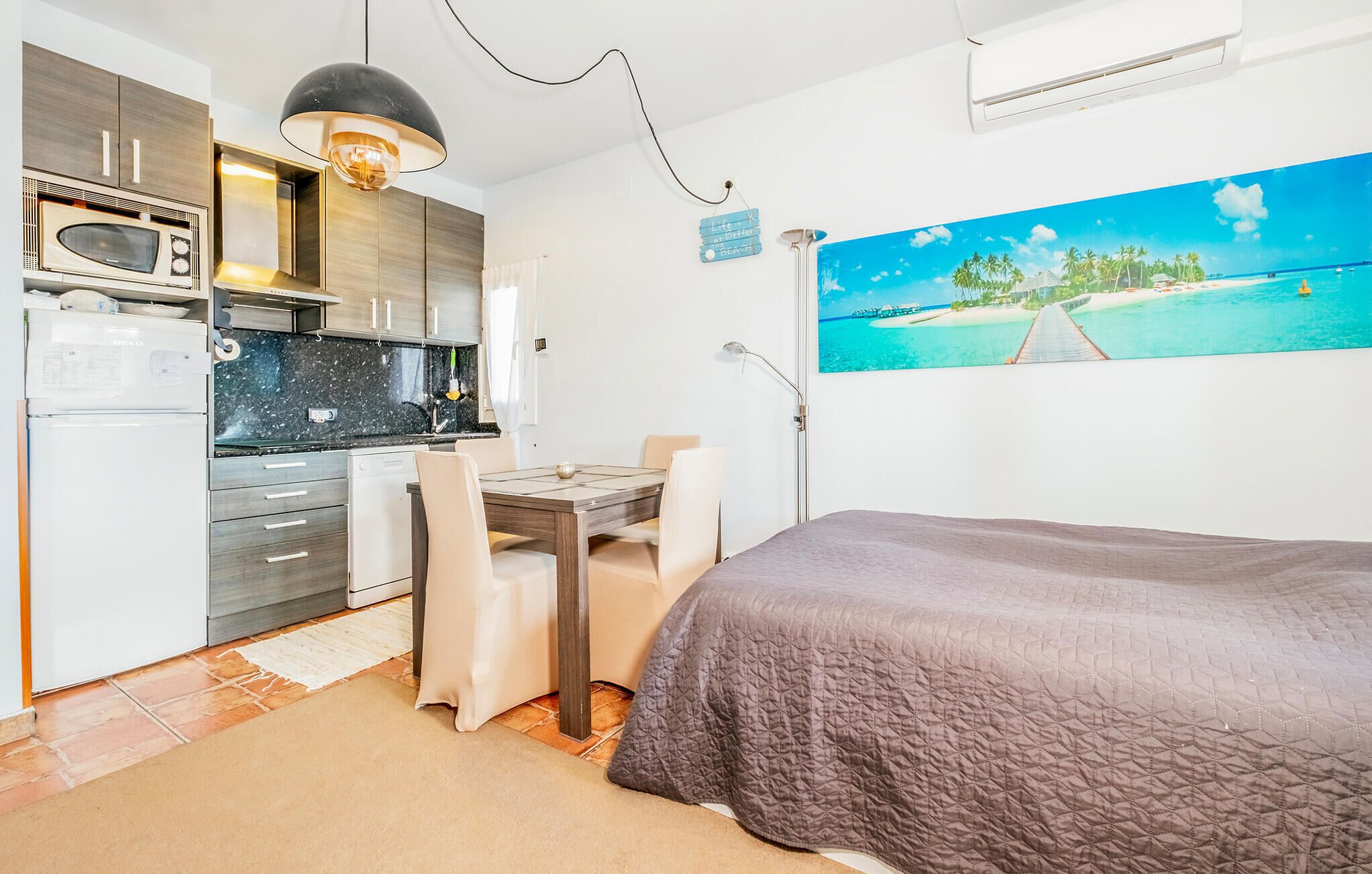 A compact room with a kitchenette, a dining area, and a bed.