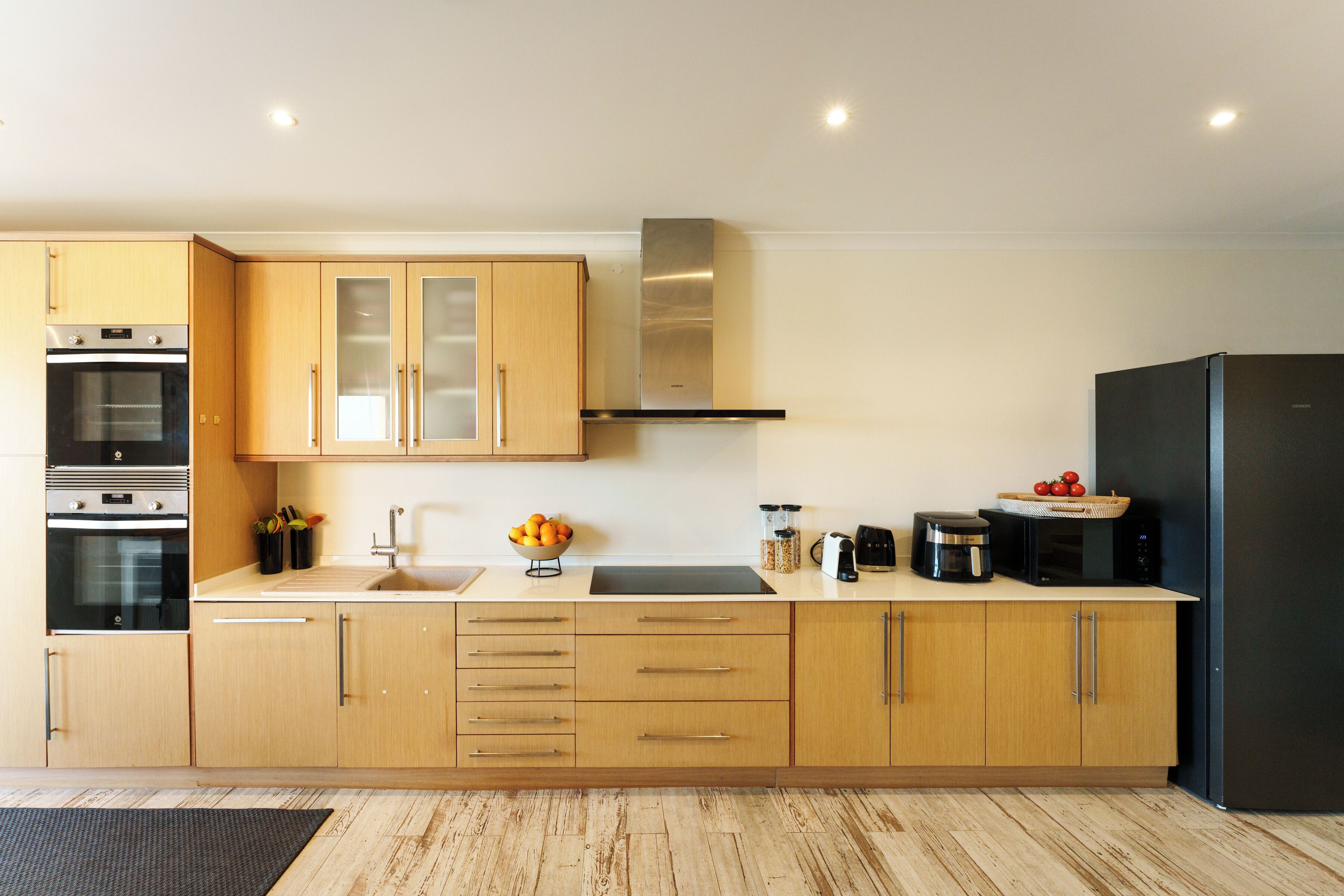 Una cocina moderna con armarios de madera, una campana extractora de acero inoxidable y un refrigerador negro.