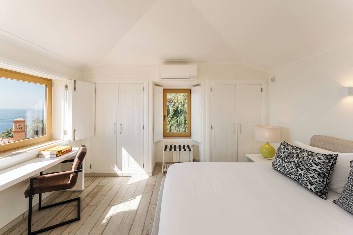 A bedroom with a bed, a desk, a chair, a window, and a view of the outdoors.