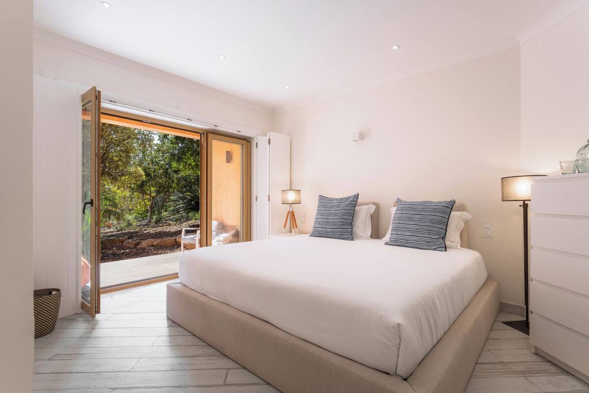 A bedroom with a large bed, bedside lamps, a view through an open door, and a floor lamp.
