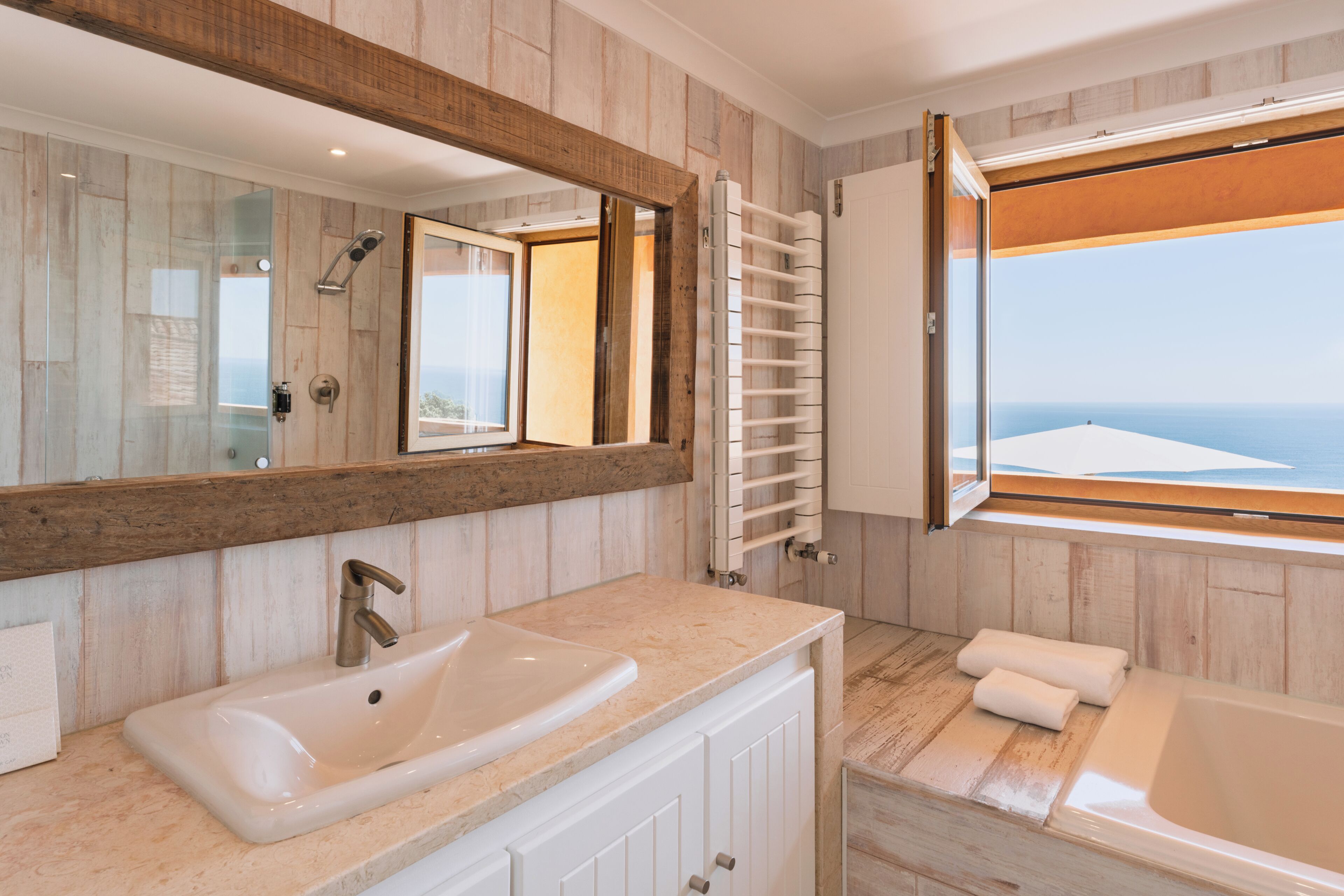 Ein Badezimmer mit großem Spiegel, Waschbecken, Dusche, Badewanne und Meerblick.