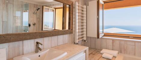 Ein Badezimmer mit großem Spiegel, Waschbecken, Dusche, Badewanne und Meerblick.