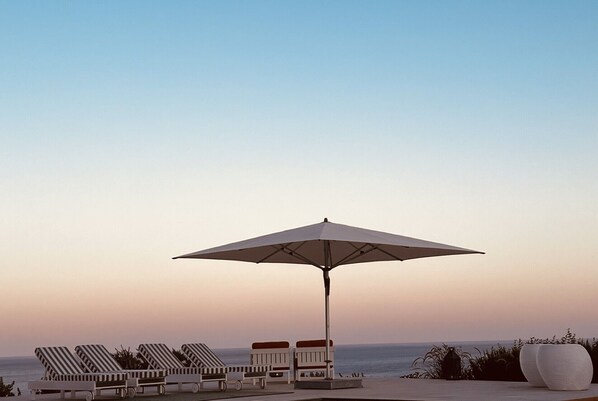 A beachside lounge area with striped lounge chairs and a large umbrella.