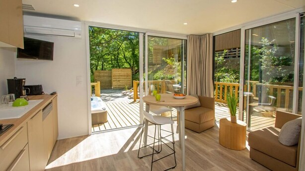 Une cuisine moderne avec un coin repas, de grandes portes-fenêtres coulissantes donnant sur une terrasse extérieure et un coin salon confortable avec un canapé et une petite table.