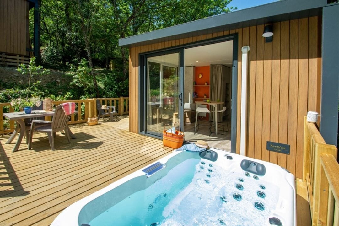 Un bain à remous sur une terrasse en bois, avec une porte vitrée donnant sur une pièce.