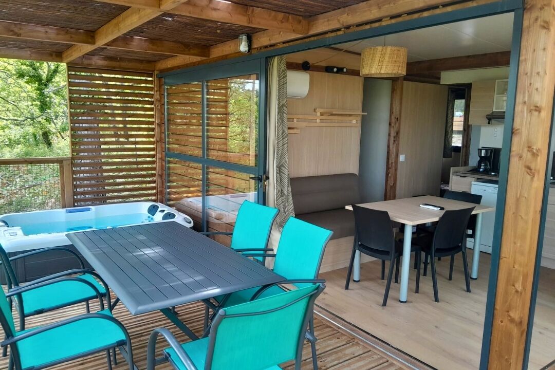 Een houten terras met een tafel, stoelen, een jacuzzi en een keukenhoek.
