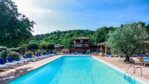 Une piscine rectangulaire à l’eau bleue, entourée de chaises longues et d’un kiosque en bois.