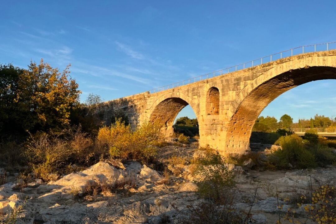 A stone bridge with three arches over a rocky terrain.