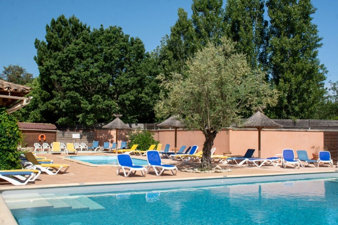 Ein Poolbereich mit mehreren Liegestühlen und Sonnenschirmen, umgeben von Bäumen und einer Backsteinmauer.