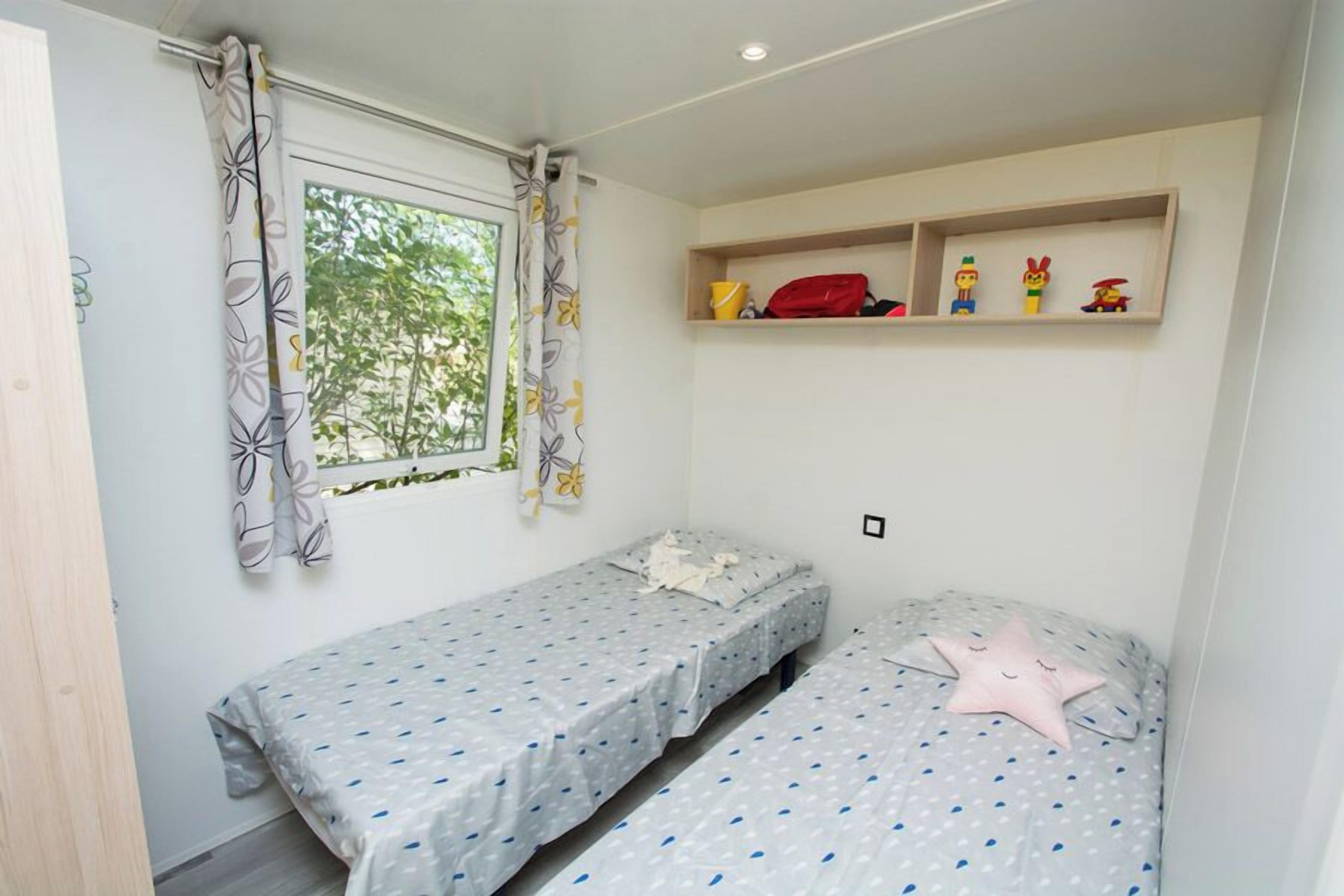 Un dormitorio con dos camas individuales, una ventana con cortinas, un estante con juguetes y una almohada con forma de estrella.