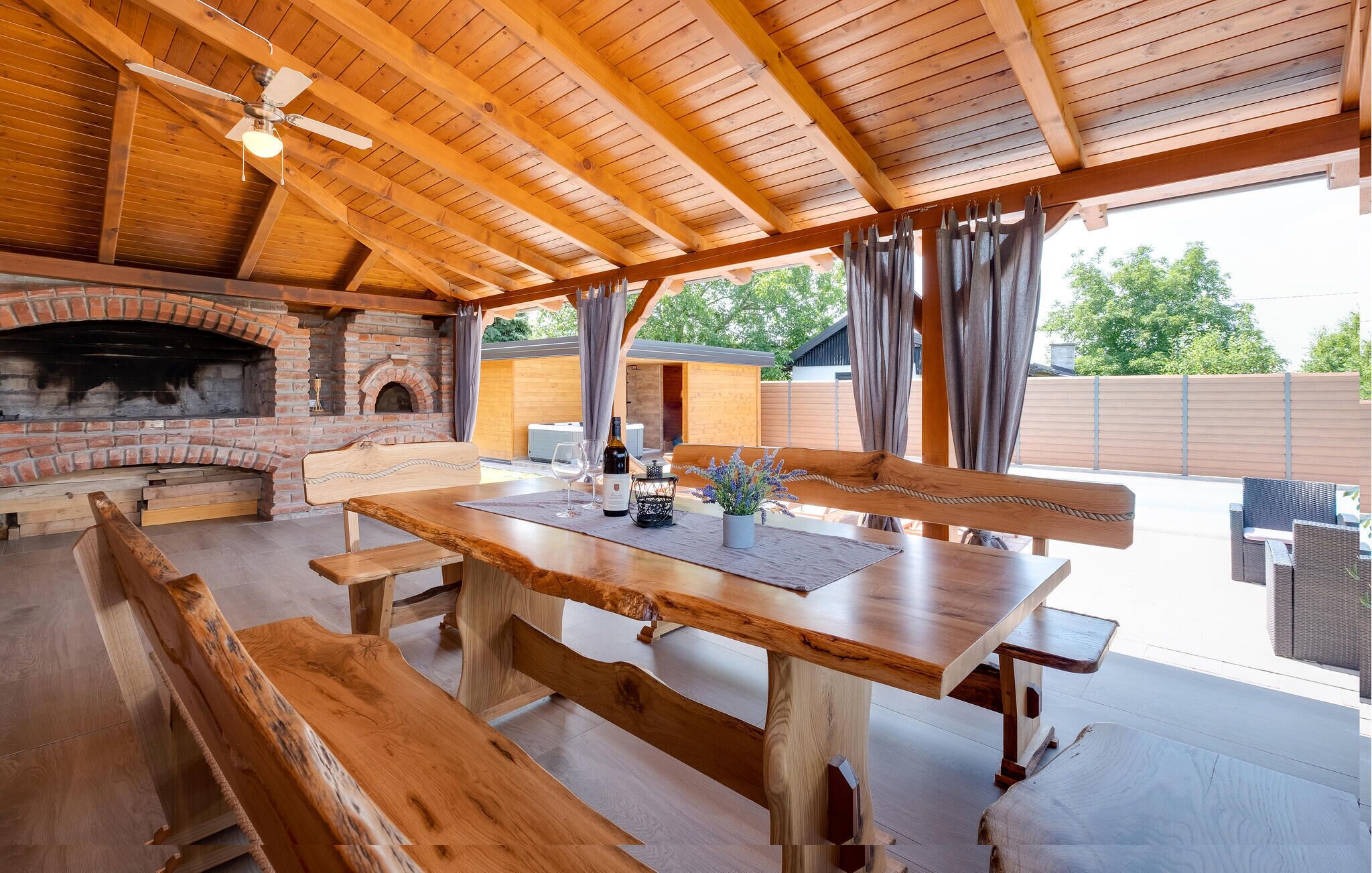 An outdoor patio with a brick fireplace, wooden benches, and a table with a wine bottle.