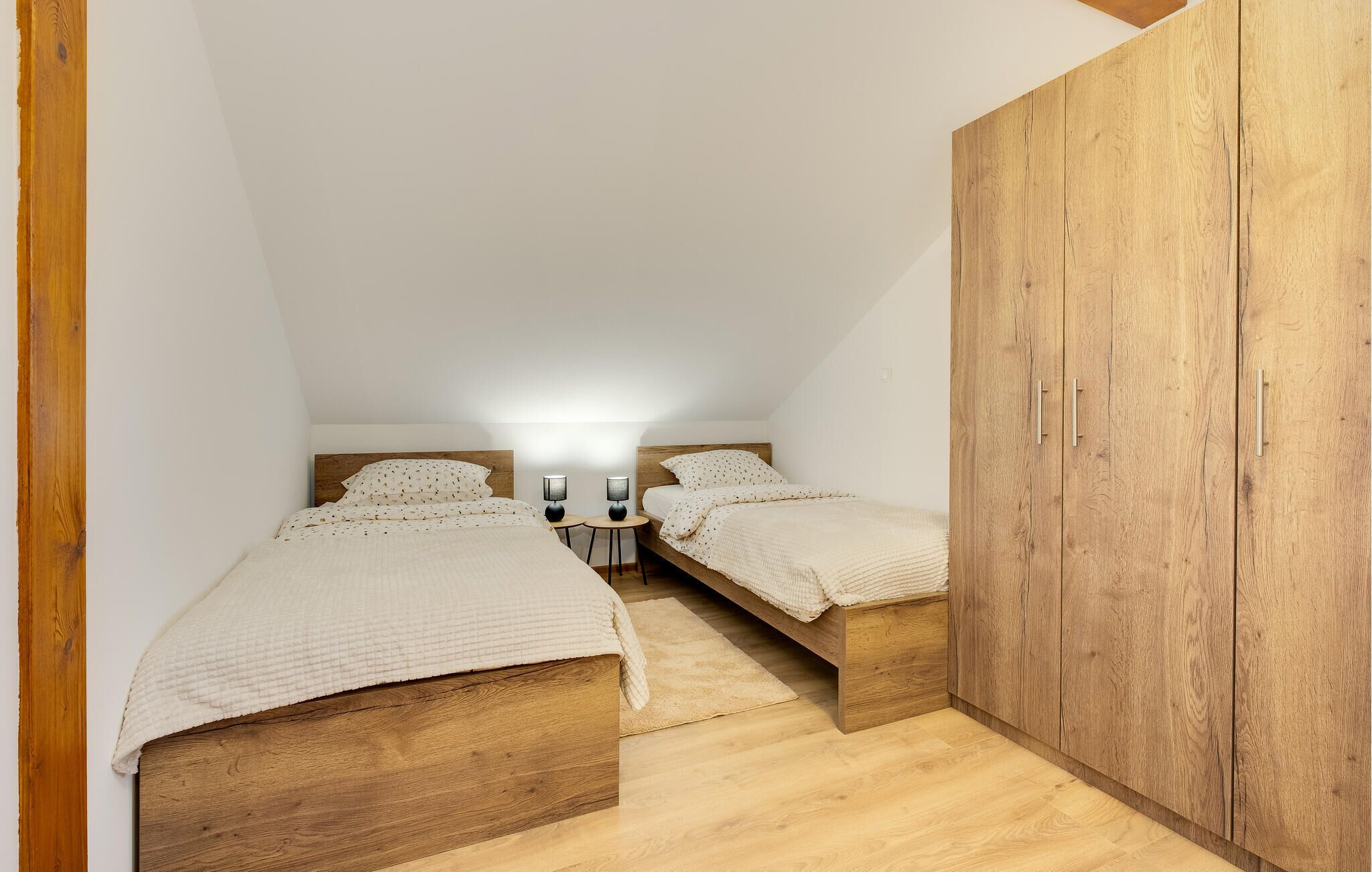 Ein kleines, gemütliches Schlafzimmer mit zwei Holzbetten, einem Nachttisch mit Lampe und einem großen Holzschrank.
