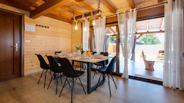 A wooden interior with a dining table set for four, black chairs, and a chandelier. - Luxurious home in Gornje Plavnice with sauna (Gornje Plavnice)