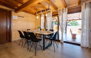Un interior de madera con una mesa de comedor preparada para cuatro personas, sillas negras y una araña.