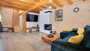 A cozy living room with a wooden ceiling, a fireplace, a sofa with cushions, a coffee table, and a TV mounted on the wall. - Luxurious home in Gornje Plavnice with sauna (Gornje Plavnice)