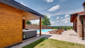 A modern outdoor pool area with a wooden deck, lounge chairs, and a hot tub. - Luxurious home in Gornje Plavnice with sauna (Gornje Plavnice)