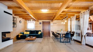 A cozy living room with a wooden ceiling, a sofa with yellow cushions, a dining table with chairs, and a fireplace. - Luxurious home in Gornje Plavnice with sauna (Gornje Plavnice)