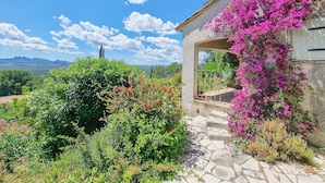 Un chemin de pierres mène à une maison d’où l’on peut admirer une vue sur les montagnes et un ciel dégagé.