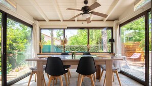 Ein Essbereich mit Holztisch und Stühlen, großen Fenstern und einem Deckenventilator.