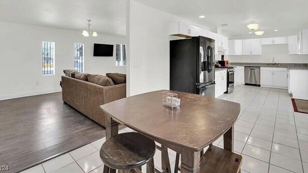 A spacious living area with a dark wooden floor, a brown sofa, a dining table with two stools, and a ceiling fan. - 4 beds 2 baths in Las Vegas
 (Las Vegas)