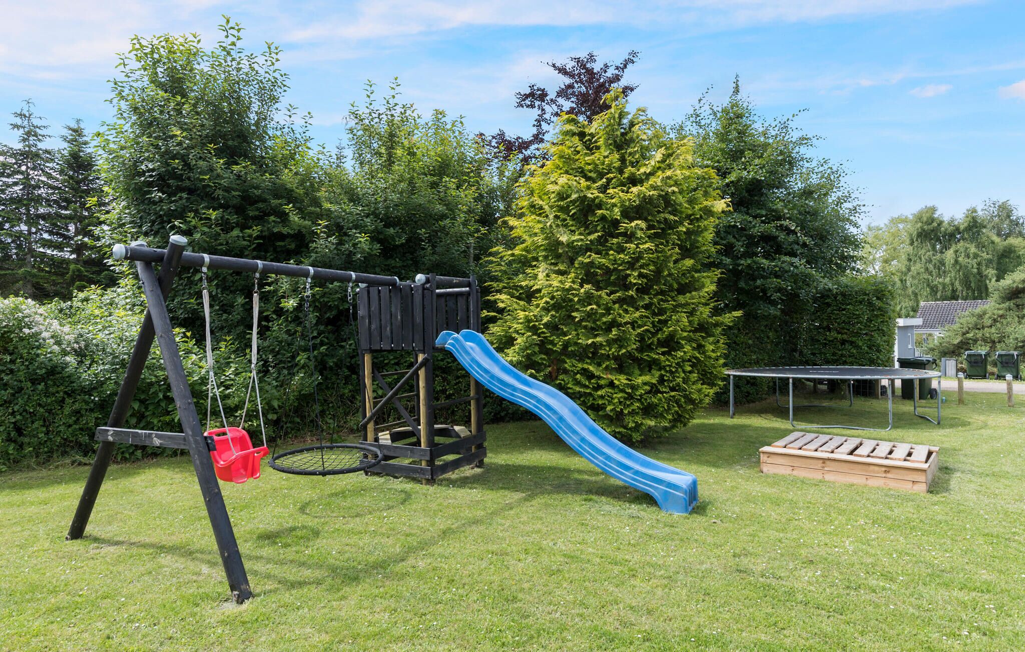 A playground with a swing set and a slide, surrounded by trees and a grassy area.