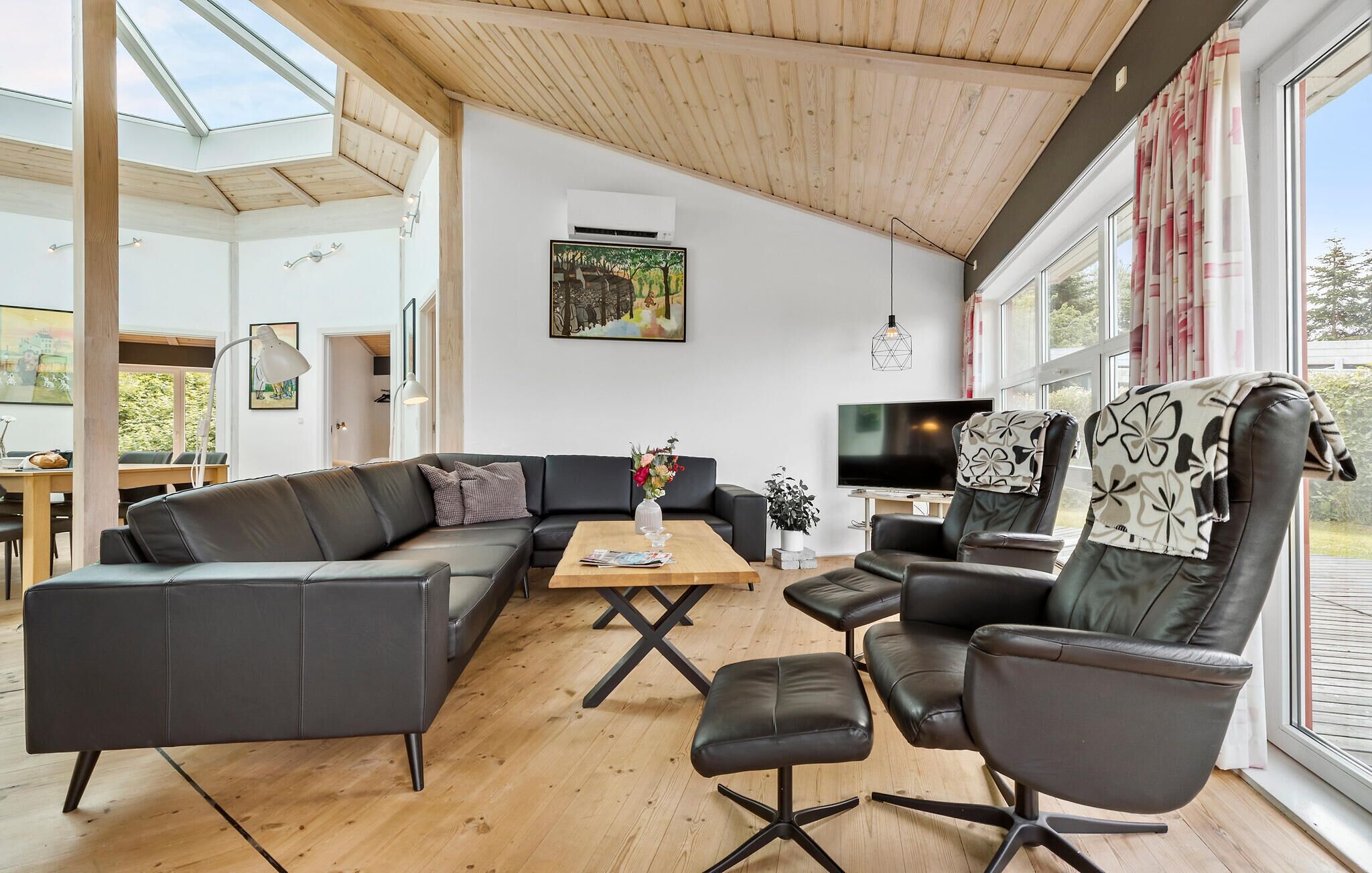 Un salon moderne avec un plafond en bois, un canapé en cuir noir, une table basse et un téléviseur.