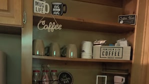 Et opbevaringsskab med kaffetema, med kaffekopper, kaffemaskine og et skilt, der siger "Coffee Bar".