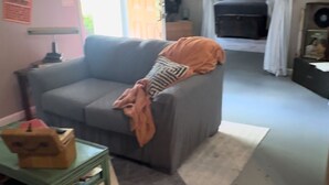 En stue med en grå sofa, et lille bord med en æske, og en dør, der fører til et andet rum.