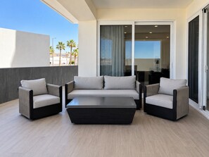 A modern outdoor seating area with a sofa and two armchairs, a coffee table, and a sliding glass door leading to an indoor space.