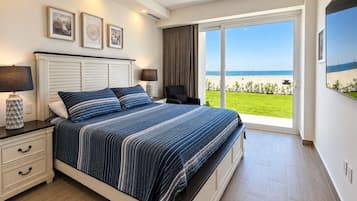 Een slaapkamer met een groot bed, een nachtkastje, een lamp en uitzicht op het strand door een schuifdeur.