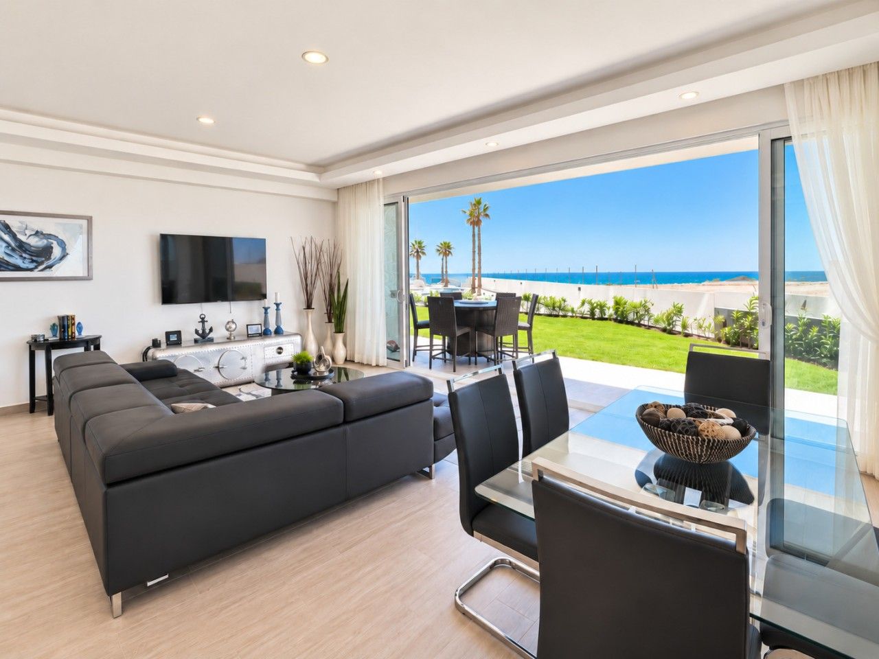 Een moderne woonkamer met een grote zwarte bank, een glazen eettafel en uitzicht op het strand.