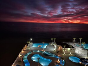 Ein Resort mit mehreren Schwimmbecken, Palmen und Blick auf den Ozean bei Sonnenuntergang.