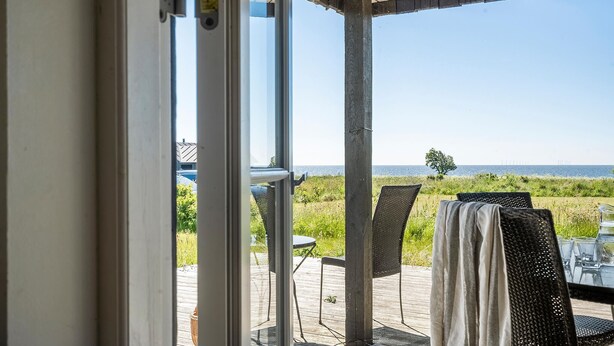 Un espacio al aire libre cubierto con vista al mar, que incluye una mesa y sillas, y una terraza de madera.