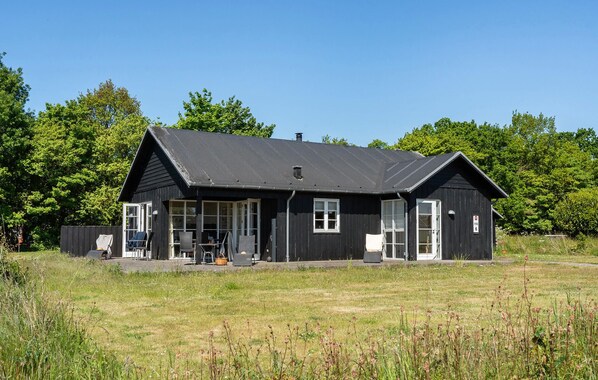 A black wooden building with a sloped roof, a porch with chairs, and a number '6' sign. - Awesome home in Nysted with house sea view (Nysted)
