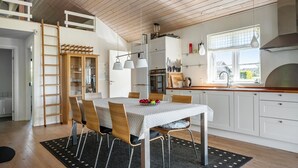 Una cocina moderna con armarios blancos, techo de madera y zona de comedor con mesa y sillas.