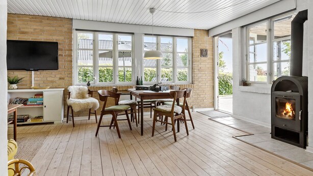 A cozy room with a fireplace, wooden flooring, and a dining area with chairs and a table. - 3 bedroom awesome home in Brenderup Fyn (Brenderup Fyn)