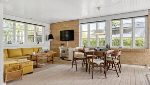 A spacious living room with a yellow sofa, wooden dining table, and chairs, large windows, and a brick wall. - 3 bedroom awesome home in Brenderup Fyn (Brenderup Fyn)