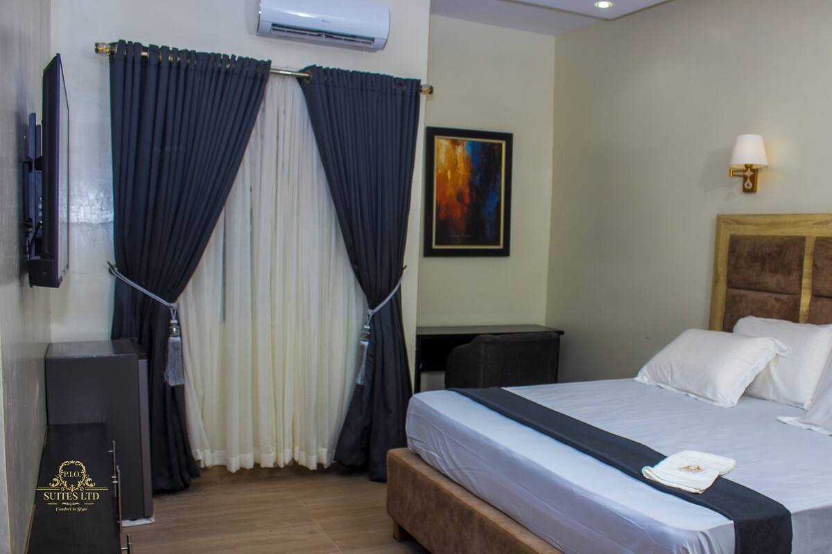 A hotel room with a bed, a TV, a desk, and a painting on the wall.