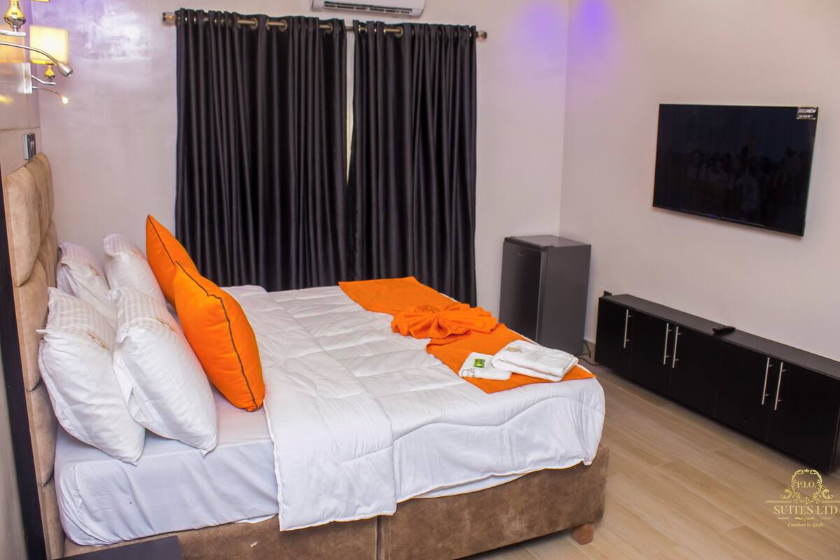 A bedroom with a bed, pillows, a TV, a speaker, and a wardrobe.