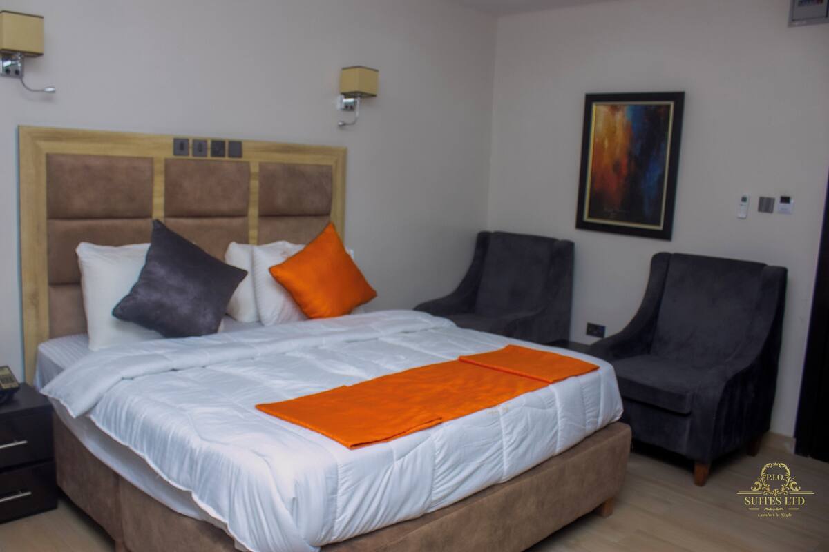 A hotel room with a large bed, two armchairs, a bedside table, and a painting on the wall.