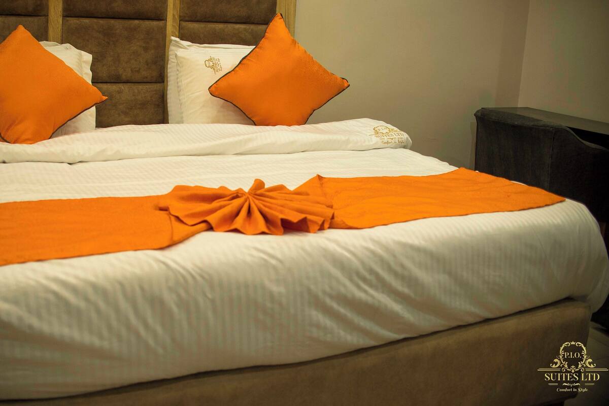 A neatly made bed with white linens and two orange pillows.