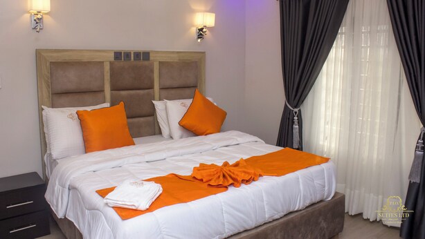A hotel room with a large bed, two wall-mounted lamps, a wooden headboard, and a window with dark curtains. - P.I.O Suites (Abraka)