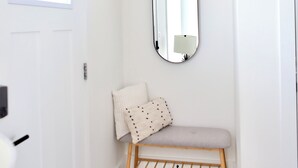 Un couloir avec une porte blanche, un banc doté d’un coussin et un miroir fixé au mur.