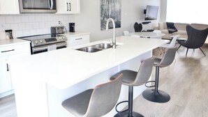 Une cuisine moderne avec des meubles blancs, des appareils en acier inoxydable et un îlot central doté de tabourets de bar.