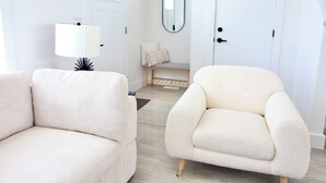 Une pièce moderne et minimaliste, avec un canapé blanc, un fauteuil confortable, une lampe, un miroir et une porte.