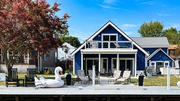 A two-story house with a balcony, a porch with chairs, and swan inflatable decorations. - !Newly Upgraded! Hot Tub-Game Room-Dock-Fire Pits (Millersport)