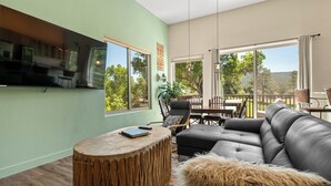 A living room with a large sectional sofa, a round wooden coffee table, and a television mounted on the wall. - Red Rock Views! Pool~Pickleball~Hike~Golf, Deck Overlooks the 9th Green! Sedona (Sedona)