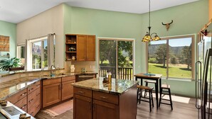 A spacious kitchen with wooden cabinets, granite countertops, and a large island. There is a dining area with a table and chairs, and a view of a golf course through large windows. - Red Rock Views! Pool~Pickleball~Hike~Golf, Deck Overlooks the 9th Green! Sedona (Sedona)