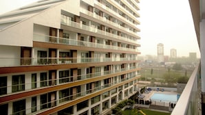 A multi-story hotel with balconies, a swimming pool, and a view of the cityscape. - Immaculate Beauty Gem Location Pools Gym (Accra)